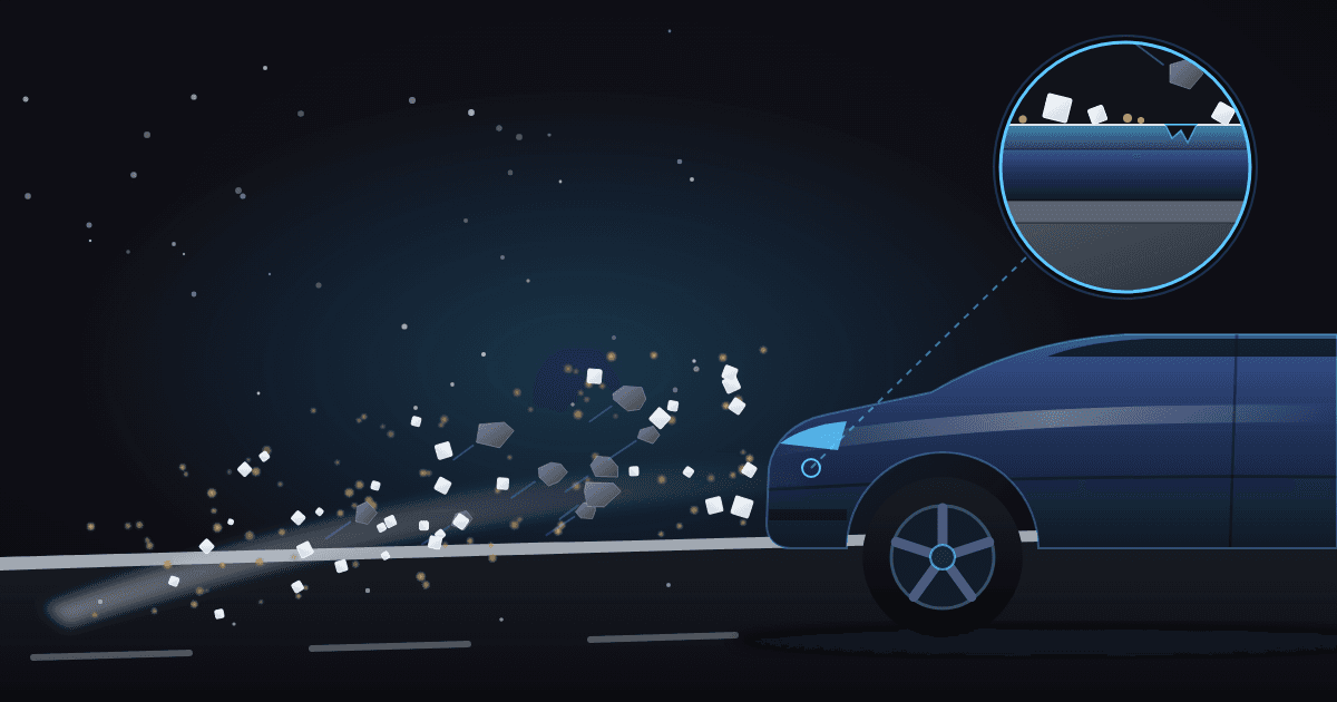 Illustration of a winter road at night with slush, white salt crystals, sand grains and small stones spraying toward the front of a generic dark blue car, and a magnified circle showing the car's paint layers with salt and grit on the surface and a small chip in the clear coat.
